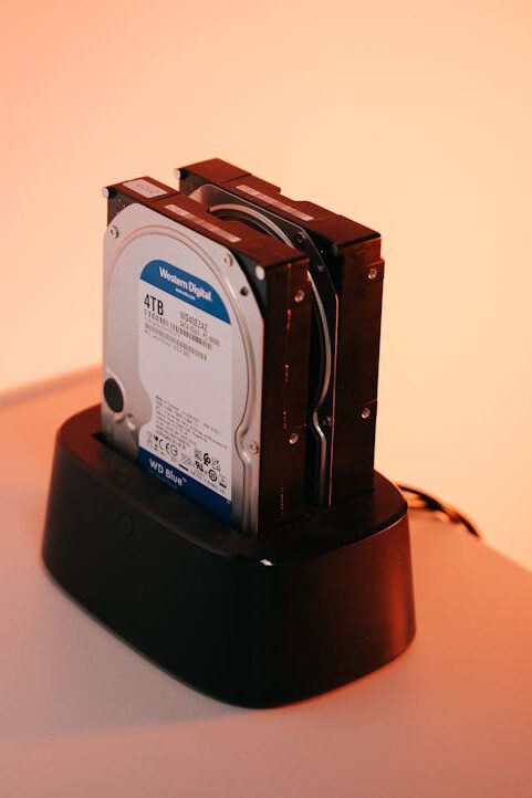 Dual external hard drives on a docking station with an orange backdrop.